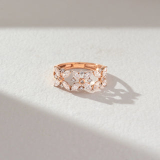 Top angled view of floral diamond band ring in rose gold, featuring marquise-shaped lab-grown diamonds forming detailed flower motifs. Set against a soft beige textured background with natural shadows.