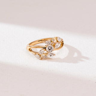 Top angle view of a 14KT yellow gold leaf-inspired diamond ring with marquise-shaped diamonds and a round center stone in an open crossover design on a polished band.