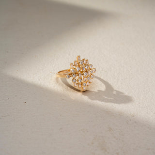 Side view of a geometric diamond statement ring in 14 KT Yellow Gold, featuring round and baguette-cut lab-grown diamonds arranged in an intricate lattice-inspired design, displayed against a beige backdrop.