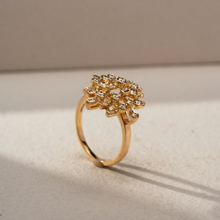 Angle view of a geometric diamond statement ring in 14 KT Yellow Gold, featuring round and baguette-cut lab-grown diamonds arranged in an intricate lattice-inspired design, displayed against a beige backdrop.