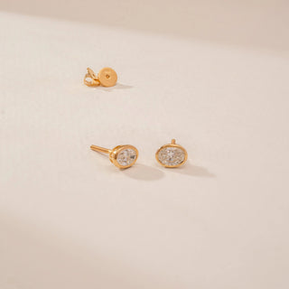 Angled view of a 14KT Yellow Gold diamond stud earrings, featuring oval diamonds in a bezel setting.