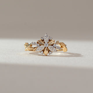 Front view of floral diamond ring in yellow gold, featuring marquise and round lab-grown diamonds arranged in a blooming flower motif with leaf-inspired details on the band. Set on a soft neutral backdrop, it reflects elegant charm.