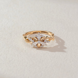 Top view of floral diamond ring in yellow gold, featuring marquise and round lab-grown diamonds arranged in a blooming flower motif with leaf-inspired band details. Set on a soft neutral surface, it reflects graceful elegance.