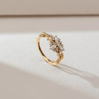 Side angled view of floral diamond ring in yellow gold, featuring marquise and round lab-grown diamonds in a blooming flower motif with leaf-inspired band details. Set on a soft neutral backdrop, it highlights intricate elegance.