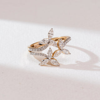 Top angle view of a 14KT yellow gold triple marquise floral diamond ring featuring three marquise-cut diamond flower motifs and a split pavé diamond band on a soft neutral surface.