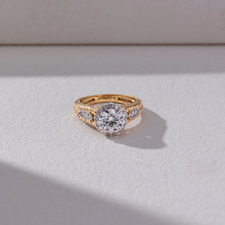 Top view of Vintage Halo Diamond Ring in 14KT Yellow Gold, featuring a round lab grown diamond with halo and engraved band details. Set on a beige backdrop, the design highlights symmetry and intricate elegance.
