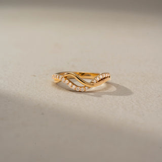 Front view of a floral crossover statement ring in 14 KT Rose Gold, featuring emerald-cut lab-grown diamond clusters, pear-shaped floral motifs, and intertwined pavé diamond bands in an open wrap design, displayed against a beige backdrop.