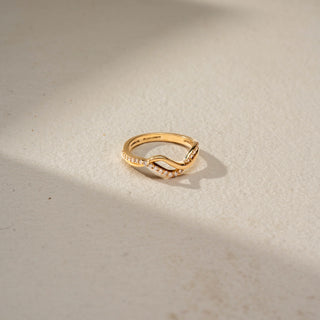 Top view of a floral crossover statement ring in 14 KT Rose Gold, featuring emerald-cut lab-grown diamond clusters, pear-shaped floral motifs, and intertwined pavé diamond bands in an open wrap design, displayed against a beige backdrop.