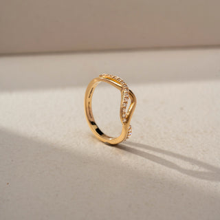 Angled view of a floral crossover statement ring in 14 KT Rose Gold, featuring emerald-cut lab-grown diamond clusters, pear-shaped floral motifs, and intertwined pavé diamond bands in an open wrap design, displayed against a beige backdrop.