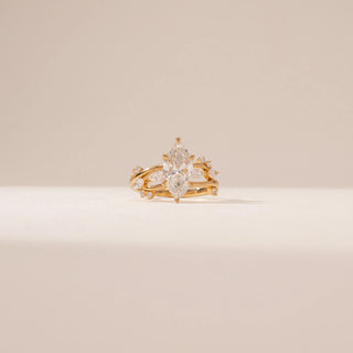 Front view of a marquise diamond ring in 14KT Yellow Gold, featuring a twisted band with marquise and round diamond accents against a beige backdrop.