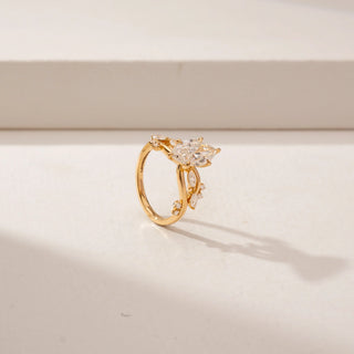Angled view of a marquise diamond ring in 14KT Yellow Gold, featuring a twisted band with marquise and round diamond accents against a beige backdrop.