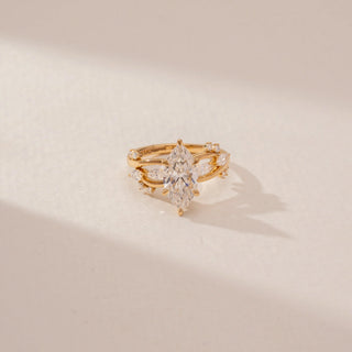 Close-up view of a marquise diamond ring in 14KT Yellow Gold, featuring a twisted band with marquise and round diamond accents against a beige backdrop.