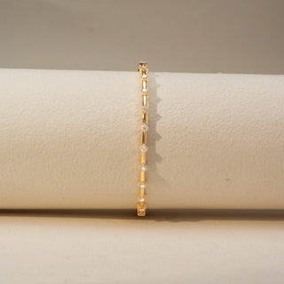 Front view of a diamond bracelet in 14 KT Yellow Gold, featuring evenly spaced round diamonds set along sleek gold links, displayed against a soft beige backdrop.
