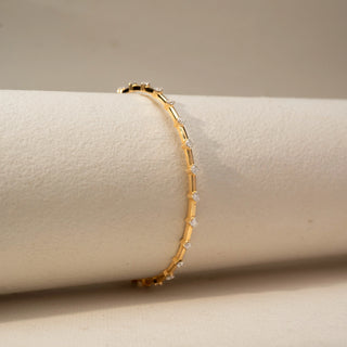 Side view of a diamond bracelet in 14 KT Yellow Gold, featuring evenly spaced round diamonds set along sleek gold links, displayed against a soft beige backdrop.