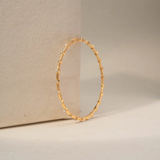 Angle view of a diamond bracelet in 14 KT Yellow Gold, featuring evenly spaced round diamonds set along sleek gold links, displayed against a soft beige backdrop.