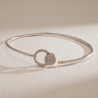 Flat lay of Sleek Circle Accent Diamond Bracelet in white gold. The bracelet highlights two interlinked circle motifs, one with pavé diamonds of EF colour and VVS clarity. The slim bangle design offers a refined, modern touch, perfect for daily elegance or gifting.