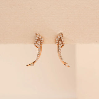 Top-down view of Reia’s 14 KT Rose Gold Graceful Arched Pavé Diamond Earrings. The layout highlights the delicate curved motif and shimmering round-cut diamonds against a cream backdrop.