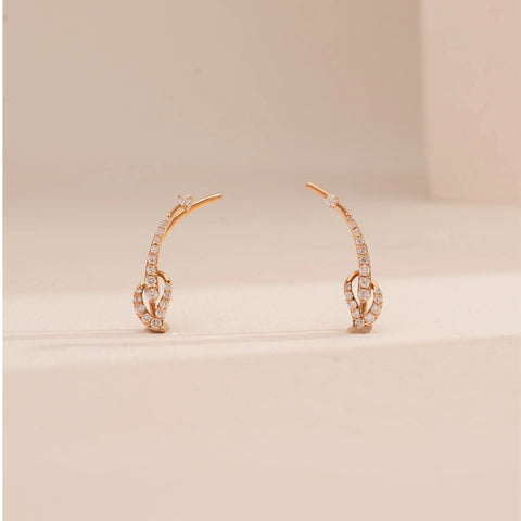 Front view of Reia’s 14 KT Rose Gold Graceful Arched Pavé Diamond Earrings. The layout highlights the fluid, arched frames pavé-set with round-cut diamonds on a clean, cream backdrop.