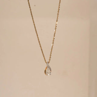 Front view of pear-shaped lab grown diamond pendant framed by a graceful gold swirl with pavé diamond accents, suspended on a fine yellow gold chain against a soft neutral background.
