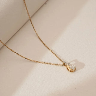 Angled view of pear-shaped lab grown diamond pendant in a flowing yellow gold swirl setting with pavé diamond accents, suspended on a fine gold chain against a soft neutral background.