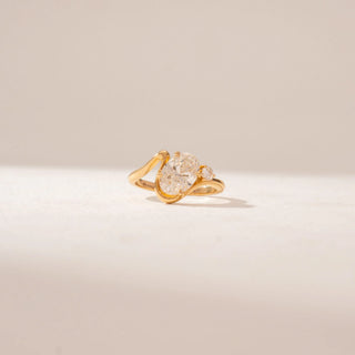 Angled view of a 14KT Yellow Gold diamond ring featuring a large oval centre diamond, a curved crossover band and a round diamond accent.