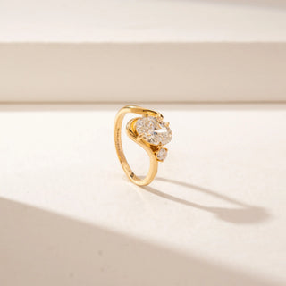 Angled view of a 14KT Yellow Gold diamond ring featuring a large oval centre diamond, a curved crossover band and a round diamond accent.