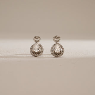 Front view of Pear Halo Drop Diamond Earrings on beige background. Crafted in 14KT hallmarked white gold with push-pull closure, featuring EF colour, VVS clarity lab grown diamonds totaling 0.94 carats, including a 0.34-carat solitaire. Product weight 2.07 grams, priced INR 50,000–1,00,000.