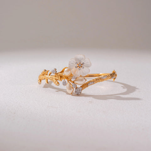 Front view of the Elegant Floral Pearl Gold Bracelet in 14KT yellow gold, featuring floral motifs with diamonds and pearl-inspired detailing. Captured against a soft beige backdrop, the design reflects timeless elegance.
