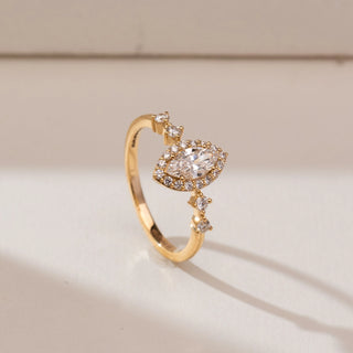 Side angle view of 14KT yellow gold ring featuring a marquise-cut centre diamond with a round diamond halo and pear-shaped accent stones along the band.