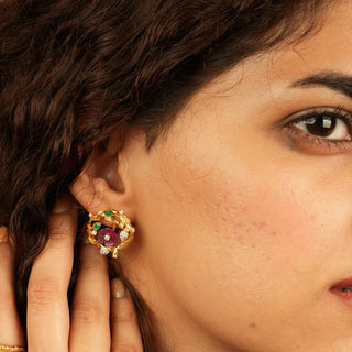 Statement stud earrings featuring a central pink stone, surrounded by green and white accents in a sculpted gold setting forming a bold floral-inspired design.