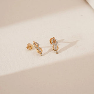 Angled view of infinity loop yellow gold diamond earrings featuring intertwined curves set with round lab grown diamonds and a delicate drop accent on a soft neutral studio surface.
