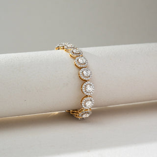Side view of Round Halo Diamond Bracelet in 14KT Dual Gold, featuring round lab grown diamonds encircled by halo settings in a continuous design. Placed on a beige backdrop, the design highlights classic brilliance and elegance.
