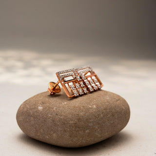 Side view of geometric diamond stud earrings in 14 KT Rose Gold, featuring pavé-set rectangular frames with floral diamond clusters, displayed on a textured stone surface.
