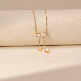 Close-up view of a 14KT yellow gold necklace featuring emerald and pear-cut diamonds, set against a beige background.