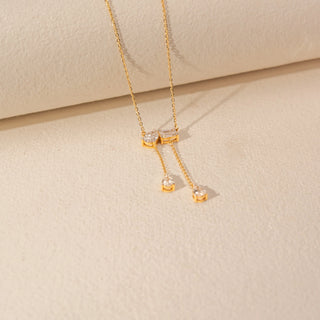 Angled view of a 14KT yellow gold necklace featuring emerald and pear-cut diamonds, set against a beige background.