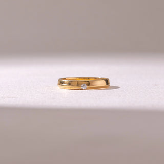Front view of a White gold diamond band ring, featuring a centred round-cut diamond set within polished bands. Captured on a soft beige backdrop, highlighting understated elegance.
