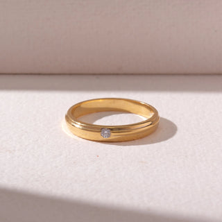 Top view of a White gold diamond band ring, featuring a centred round-cut diamond set within smooth polished bands. Captured on a soft beige backdrop, highlighting minimal elegance.
