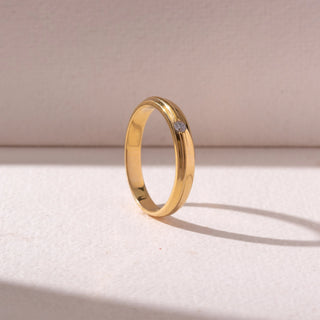 Angled view of a White gold diamond band ring, featuring a round-cut diamond set within sleek polished bands. Captured on a soft beige backdrop, highlighting refined minimalism and shine.