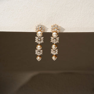 Front view of diamond and pearl drop earrings in 14 KT Yellow Gold, featuring floral diamond clusters, lustrous pearl accents, and cascading gemstone-inspired motifs against a neutral backdrop.
