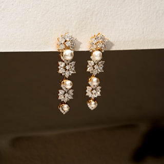 Angled view of diamond and pearl drop earrings in 14 KT Yellow Gold, featuring floral diamond clusters, lustrous pearl accents, and cascading motifs against a neutral backdrop.
