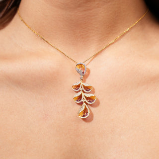 An exquisite female pendant modeled on a neckline weighing 5.13 grams, crafted from 14 KT yellow gold, it features a stunning 1.01 carat lab-grown diamond, beautifully framed by intricate gold settings adorned with vibrant orange and purple pattern, creating a captivating display. The pendant hangs gracefully from a delicate gold chain, highlighting its leaf-like appeal.