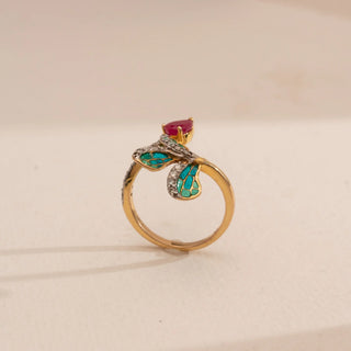 Top-down view of Reia’s 14 KT Yellow Gold Elegant Ruby Enamel Diamond Ring. It highlights the gold band, vibrant teal enamel accents, and a pear-shaped ruby center stone against a cream backdrop.