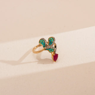 Front view of Reia’s 14 KT Yellow Gold Elegant Ruby Enamel Diamond Ring. It features a pear-shaped ruby, round brilliant diamonds, and teal enamel accents on a cream backdrop.