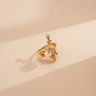 Top-down view of Reia’s 14 KT Yellow Gold Carved Floral Motif Diamond Ring. It highlights the diamond-accented flower heart and the fluid, architectural branch motif on a cream backdrop.