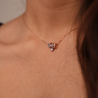 A model styling a necklace of 16 inches with a spring lock showcasing a 14 KT rose gold necklace featuring an intricate design of interlocking loops along with lab-grown round cut diamonds in a prong setting with a total of 0.41 carat with a solitaire suspended below the loops finishing with a delicate rose gold chain complimenting the pendant, weighing 3.92 grams making it a perfect piece of luxury for any occasion.