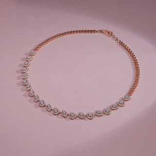 Overhead product display of a Réia lab grown diamonds necklace in rose gold, featuring alternating pear and marquise-shaped halo links with round-cut detailing, arranged on a soft blush background.