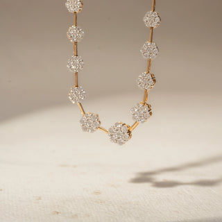 Front view of a floral diamond station necklace in 14 KT Yellow Gold, featuring round flower-shaped lab-grown diamond clusters linked along a delicate chain, displayed against a beige backdrop.
