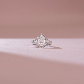 Front view of pear-shaped halo diamond ring in white gold, featuring a central lab-grown diamond with pavé-set halo and split band. Captured against a soft pink background with gentle shadows.