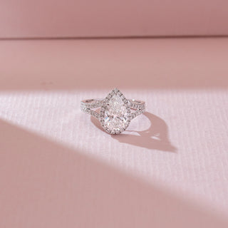 Top angled view of pear-shaped halo diamond ring in white gold, featuring a central lab-grown diamond with pavé-set halo and split band. Set against a soft pink textured background.