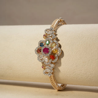 Close Up view of a multicolour gemstone and diamond bracelet in 14 KT Yellow Gold, featuring a floral cluster of vibrant gemstones framed by pavé-set diamonds, displayed against a soft beige backdrop.
